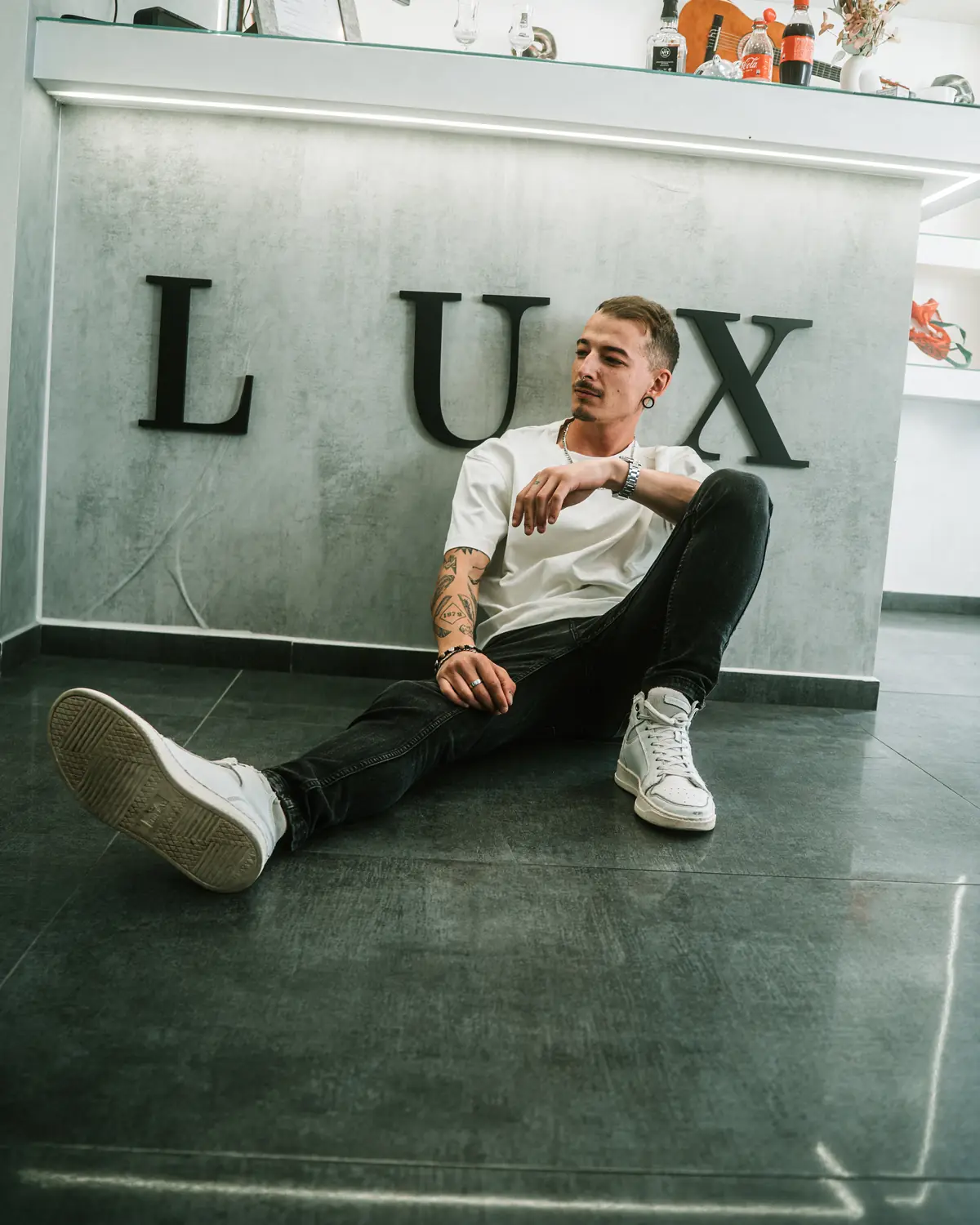 Barber sjedi na podu studija ispred zida s natpisom LUX.