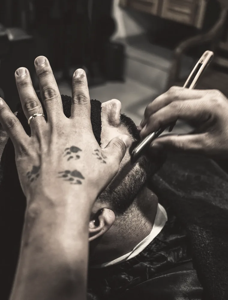 Barber pridržava glavu klijenta dok britvom radi konturu brade.