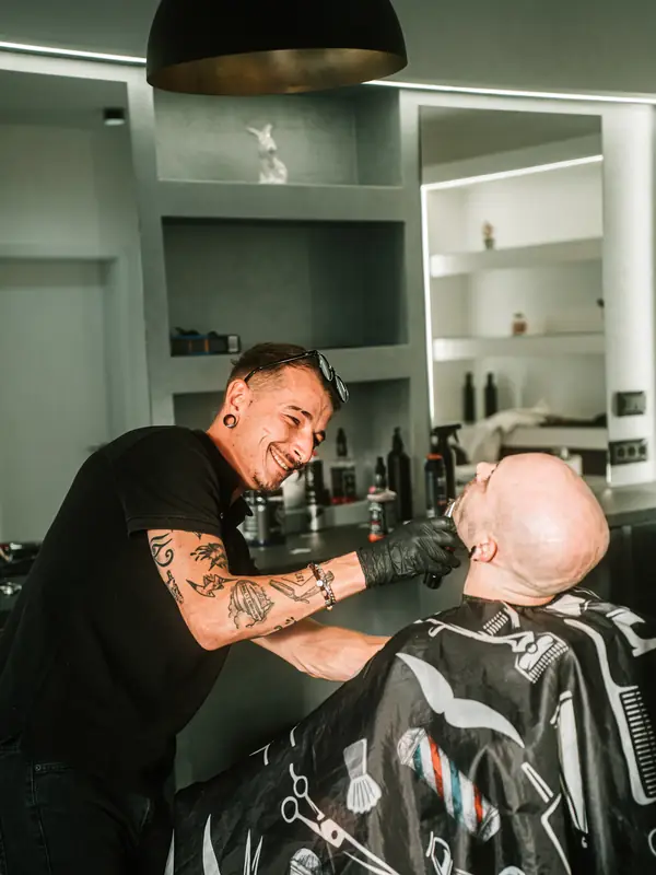 Barber se smije dok klijentu uređuje bradu.